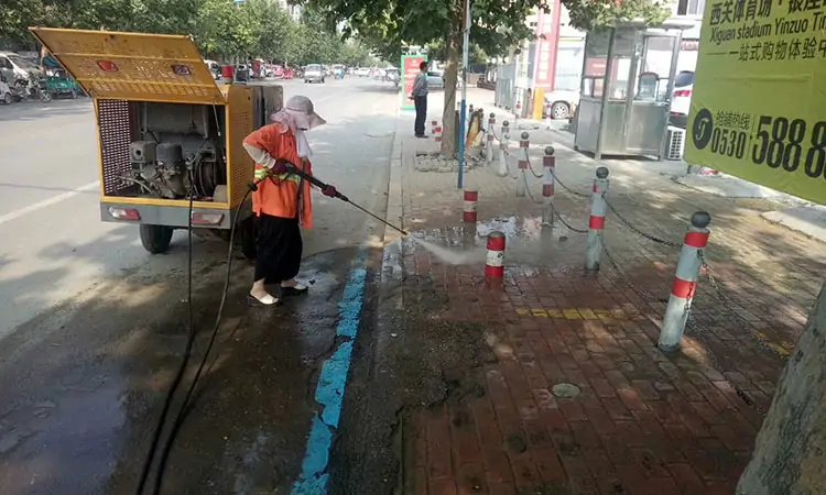 A high-pressure cleaner is washing the pavement tiles